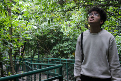 Portrait of young man looking away against trees