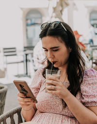 Young woman sitting on terrace of a cafe, using mobile phone