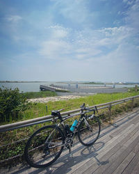 Bicycles on railing by sea against sky