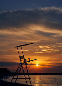 Silhouette crane by sea against sky during sunset