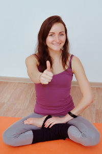 Portrait of a smiling young woman sitting against wall