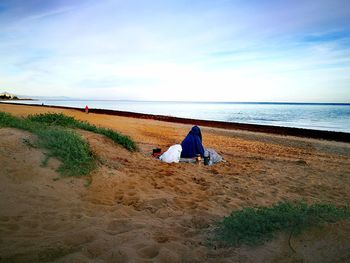 Person sitting against sky at beach