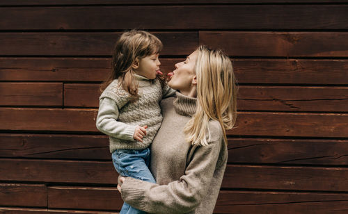 Mother holds her little daughter in her arms.  mother and daughter stuck out their tongues.