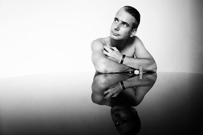 Thoughtful man sitting with reflection on table against white background