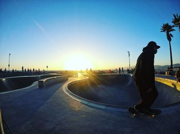 Man skateboarding on road against sky during sunset