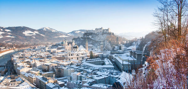 Snow covered townscape by river against clear sky