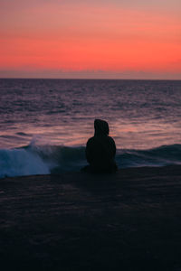 Rear view of man sitting on shore during sunset