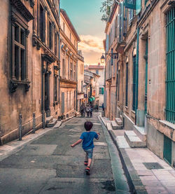 Rear view of boy walking on street amidst buildings in city