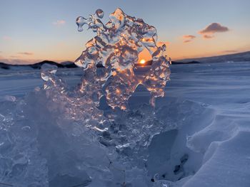 Frozen sea shore against sky during sunset