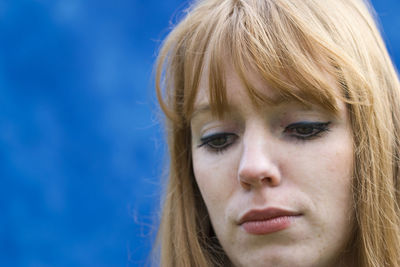 Close-up of thoughtful woman against blue wall
