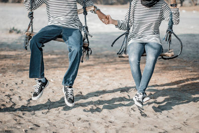 Low section of couple holding hands while swinging at beach