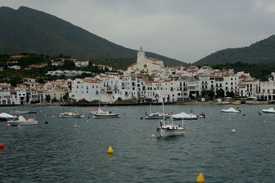 Sailboats in town by buildings in city against sky