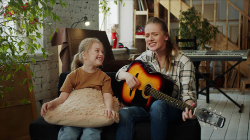 Mother singing while playing guitar with daughter at home