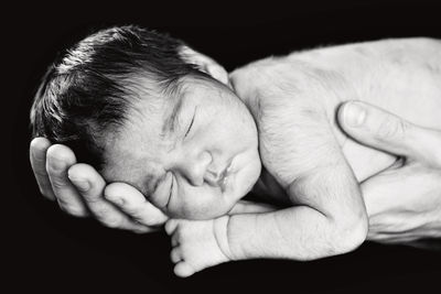 Close-up of hands holding baby girl against black background