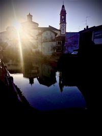 Silhouette buildings by canal against sky during sunset