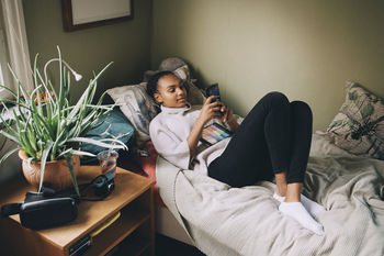 Female teenager using mobile phone while lying on bed at home