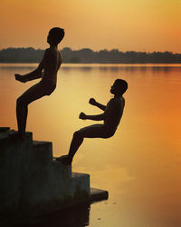 Silhouette man jumping on lake against sky during sunset