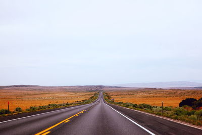 Vanishing road amidst field against clear sky