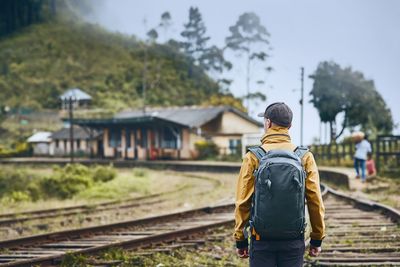 Rear view of man standing with backpack on railroad track