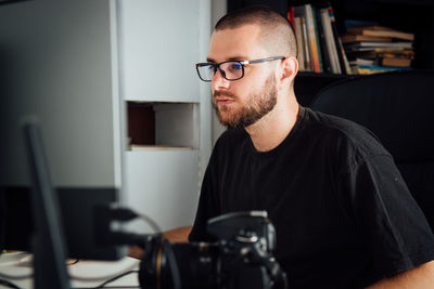 Side view of young man using computer while on chair at home