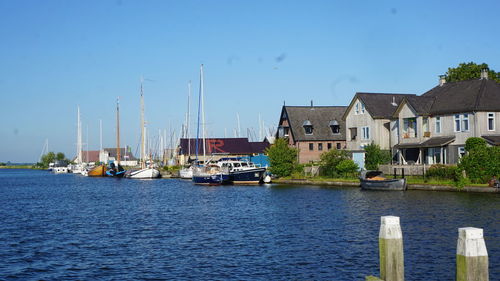 Sailboats moored on river by buildings against blue sky