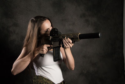 Young woman holding camera while standing against black background