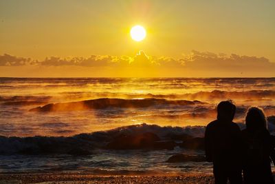 Rear view of silhouette people standing at beach during sunset