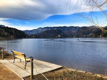 Empty bench by lake against sky