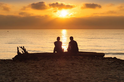 Silhouette people on beach against sky during sunset