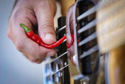 Cropped image of man plucking guitar with red chili