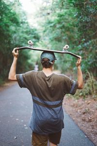 Rear view of man carrying skateboard