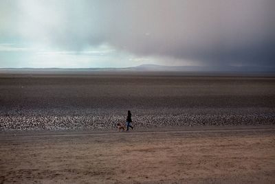 Woman with dog walking on landscape against sky