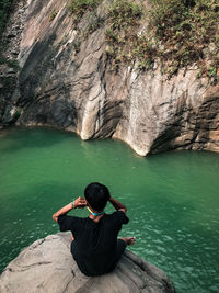 Rear view of man sitting on rock by lake