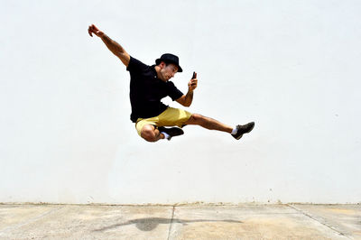 Man using smart phone while jumping against wall