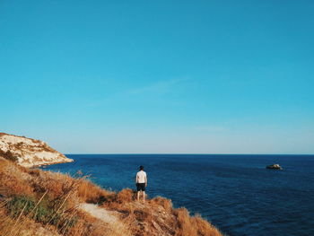 Rear view of man standing by sea against clear blue sky