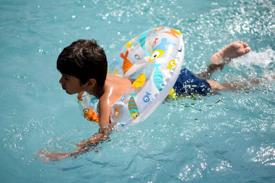 Happy indian boy swimming in a pool, kid wearing swimming costume along with air tube during day