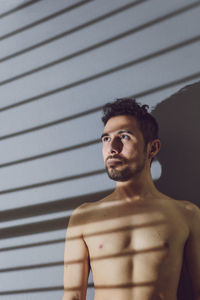 Portrait of shirtless man standing against wall