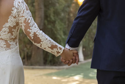 Midsection of newly wed couple holding hands outdoors