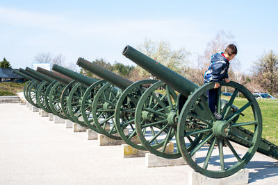 Side view of boy standing on cannons in a row