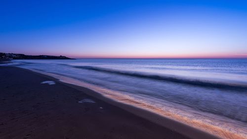 Scenic view of beach against clear sky at sunset