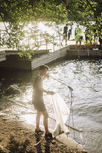 Full length side view of boy picking up rope from lake on shore