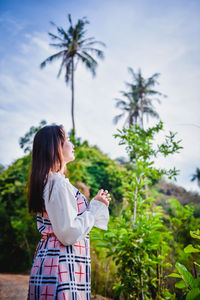 Young woman standing on palm tree against sky