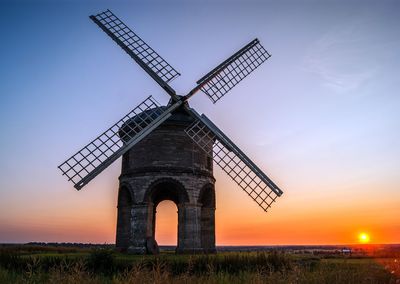 Traditional windmill on grassy field against sky during sunset