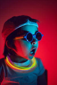 Cyberpunk boy child in white t shirt and sunglasses neon sticks on neck listening music on wall