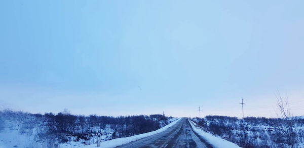 Road amidst snow covered trees against blue sky