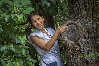 Portrait of smiling woman standing by tree in forest