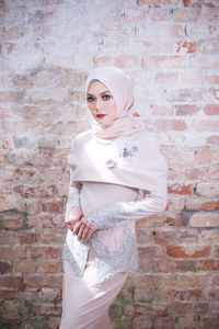 Portrait of beautiful young woman standing against brick wall