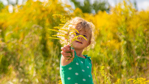 Portrait of young woman standing amidst flowering plants on field