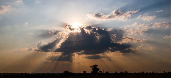 Low angle view of sunlight streaming through clouds during sunset