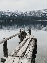 Wooden posts in lake against snowcapped mountains